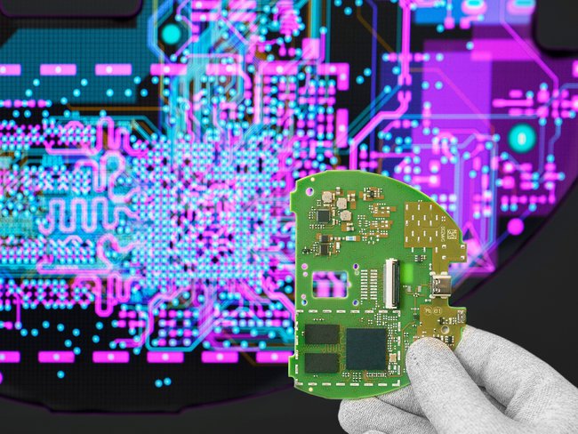Cicor engineer holding a PCB in front of a screen displaying the PCB design