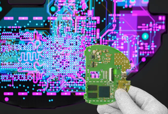 Cicor engineer holding a PCB in front of a screen displaying the PCB design